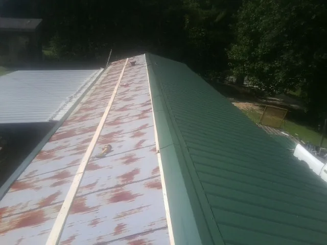 Old rusted panels beside newly installed green metal roofing — Wind Damage Roof Repair by Roofing Brothers in Evans