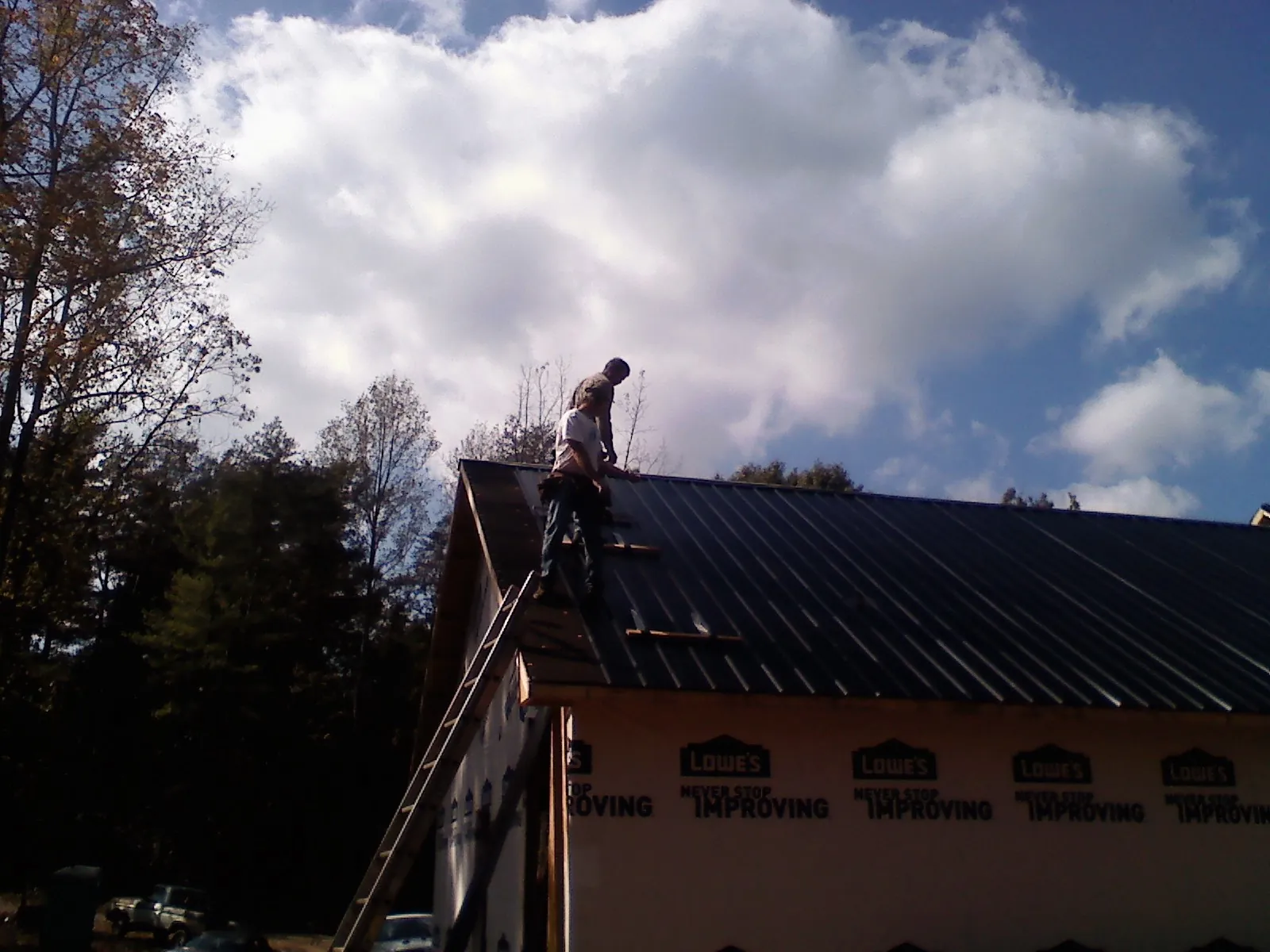 Roofer fastening dark metal panels high against a cloudy sky, from a Roof Inspection job in Evans