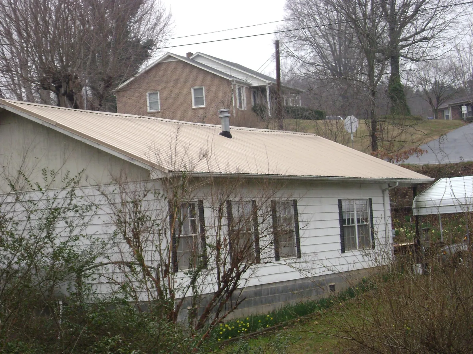 Tan metal roof on a white sided house set into a hillside — Commercial Roofing by Roofing Brothers in Evans